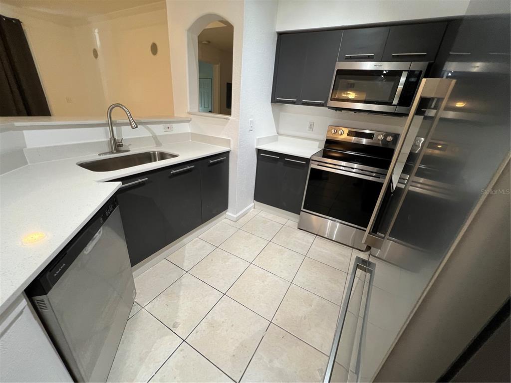 A kitchen features dark gray cabinets, stainless steel appliances, white countertops, and light tile flooring — 6685 QUEENS BOROUGH AVENUE UNIT 101, ORLANDO, FL