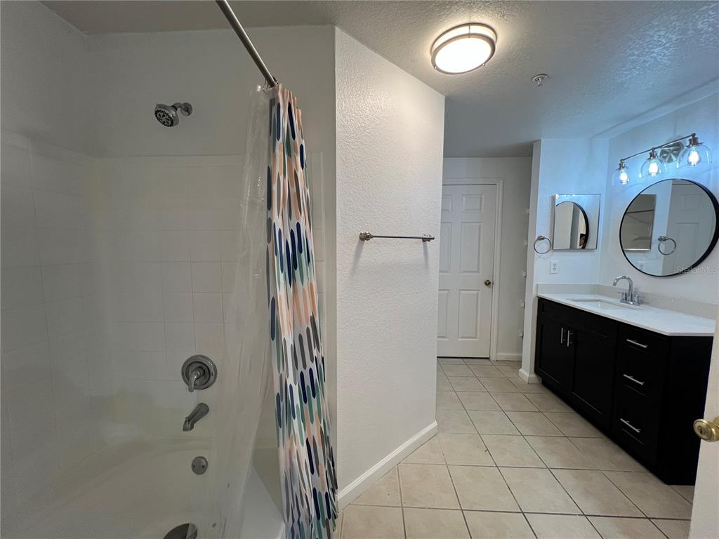 A bathroom features a shower-tub combination, a dark vanity with a mirror, and tiled flooring — 6685 QUEENS BOROUGH AVENUE UNIT 101, ORLANDO, FL