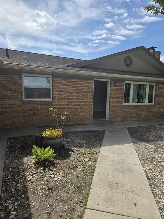 A brick house exterior features a concrete walkway leading to an open front doorway — 1420 SIMMONS ROAD, KISSIMMEE, FL