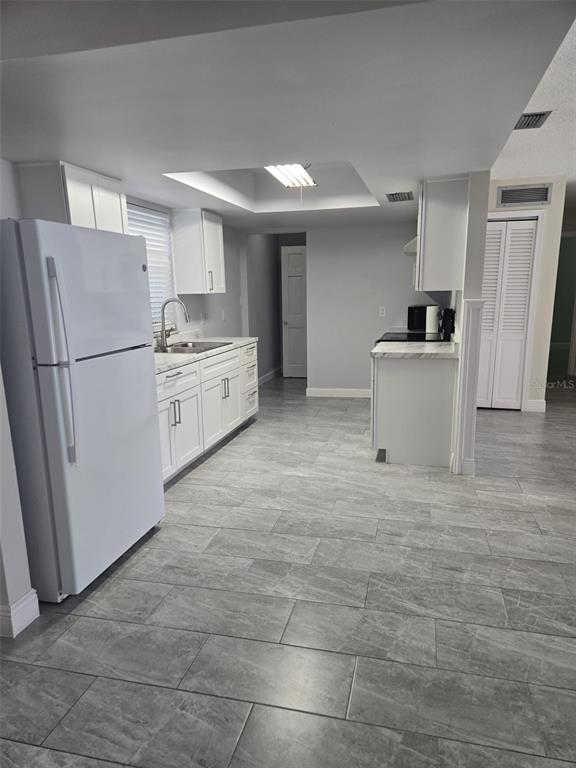 A kitchen features white cabinets, marble-look countertops, and gray tile flooring — 1420 SIMMONS ROAD, KISSIMMEE, FL