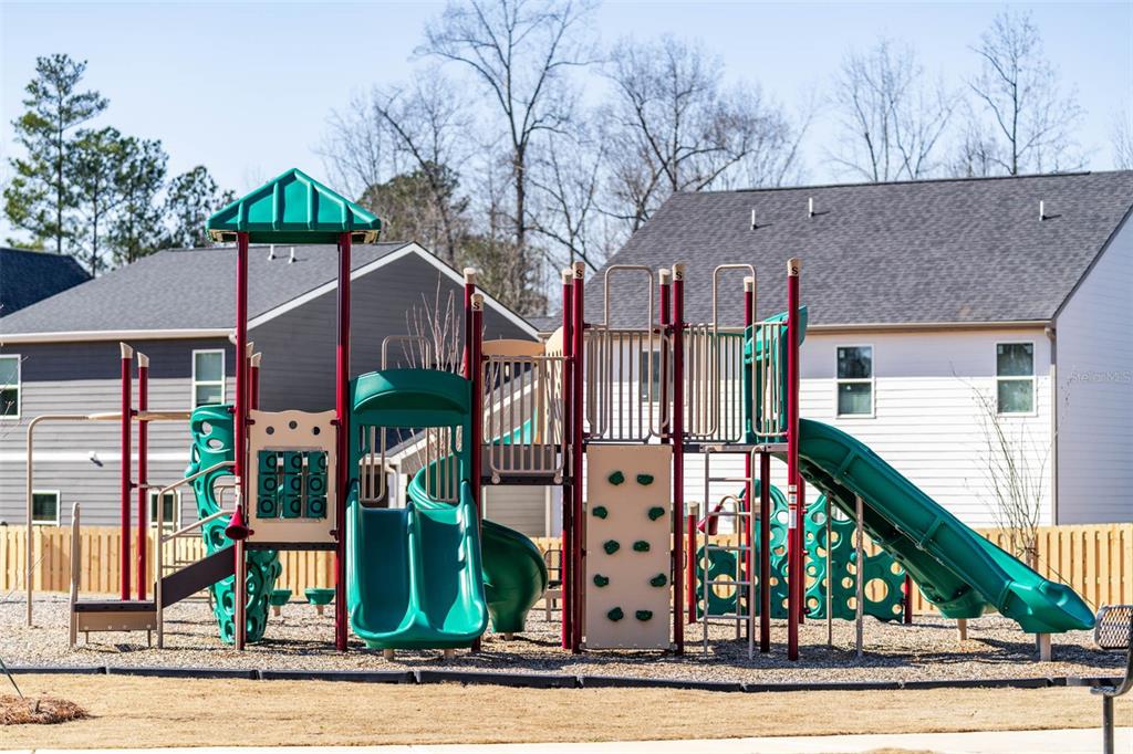 A colorful playground structure with slides and climbing walls sits on a wood-chipped surface — 7304 TOLAR ROAD, FAIRBURN, GA