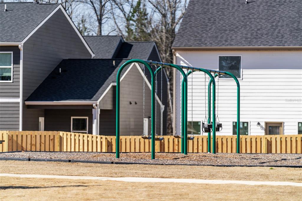 A green metal swing set stands in a playground area in front of residential houses — 7304 TOLAR ROAD, FAIRBURN, GA