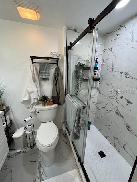 A bathroom features a toilet, a walk-in shower with marble-look tile, and a sliding door — 406 S CEDAR AVENUE UNIT 107, TAMPA, FL