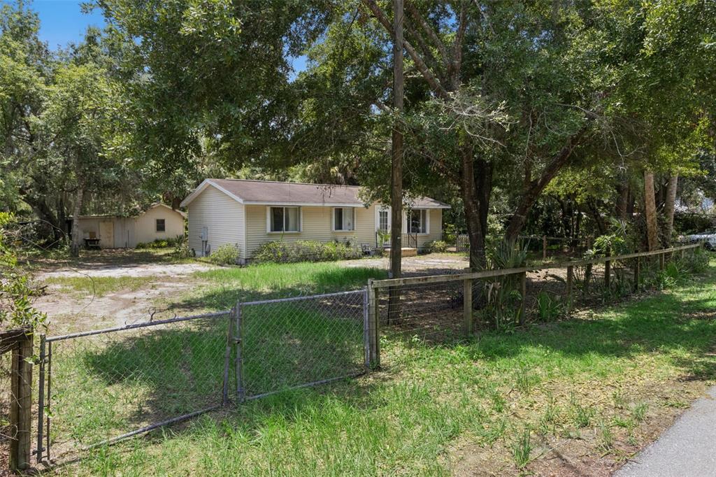 A single-story house with light-colored siding sits behind a chain-link fence among many trees — 3803 YOUNG ROAD, LAKE WALES, FL