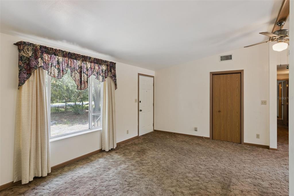 A living room with beige carpet, a large window with floral valance, and a wooden door — 3803 YOUNG ROAD, LAKE WALES, FL