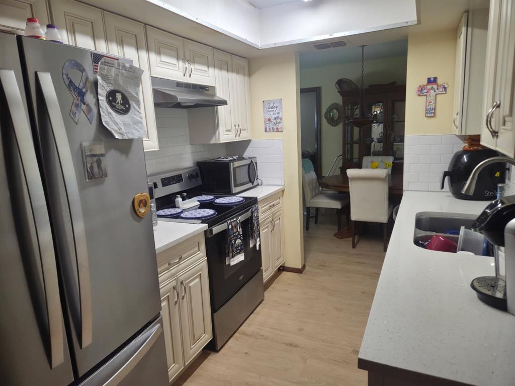 A kitchen with white cabinets, stainless steel appliances, and light wood-look flooring — 9241 TOBY LANE, ORLANDO, FL
