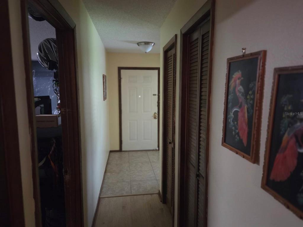 A hallway with light walls, tile flooring, louvered closet doors, and framed bird artwork — 9241 TOBY LANE, ORLANDO, FL