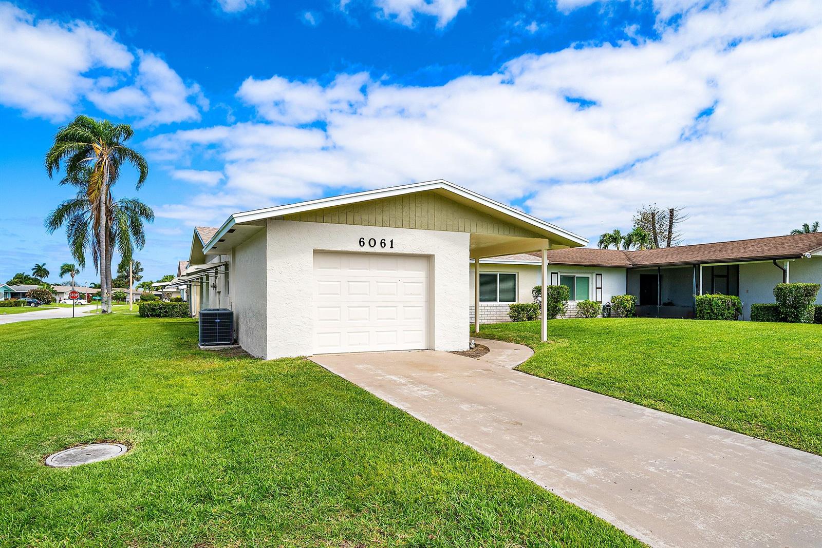A single-story house features a white garage, a concrete driveway, and a green lawn — 6061 Stanley Lane, Delray Beach FL 33484, DELRAY BEACH, FL