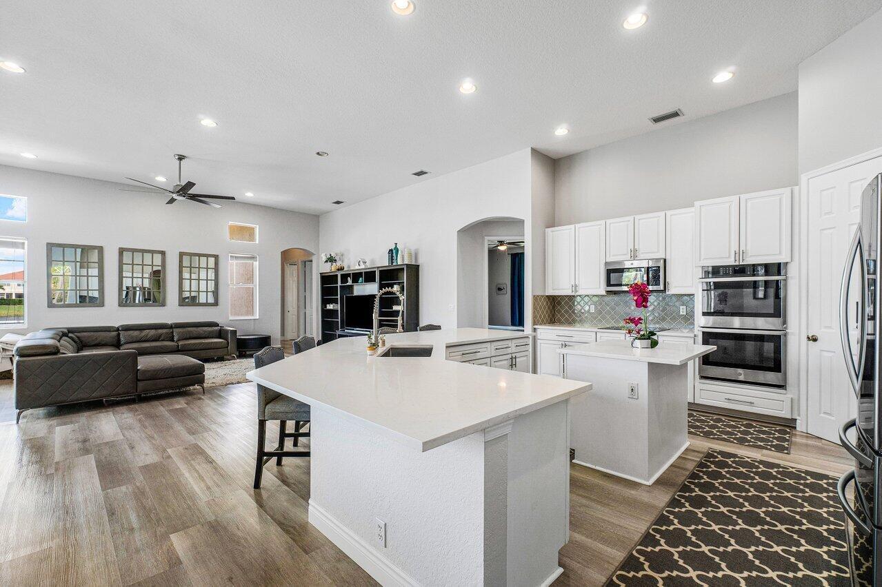 A modern open-concept kitchen and living area featuring white cabinetry, quartz countertops, and wood flooring — 11750 Osprey Pointe Circle, Wellington FL 33449, WELLINGTON, FL