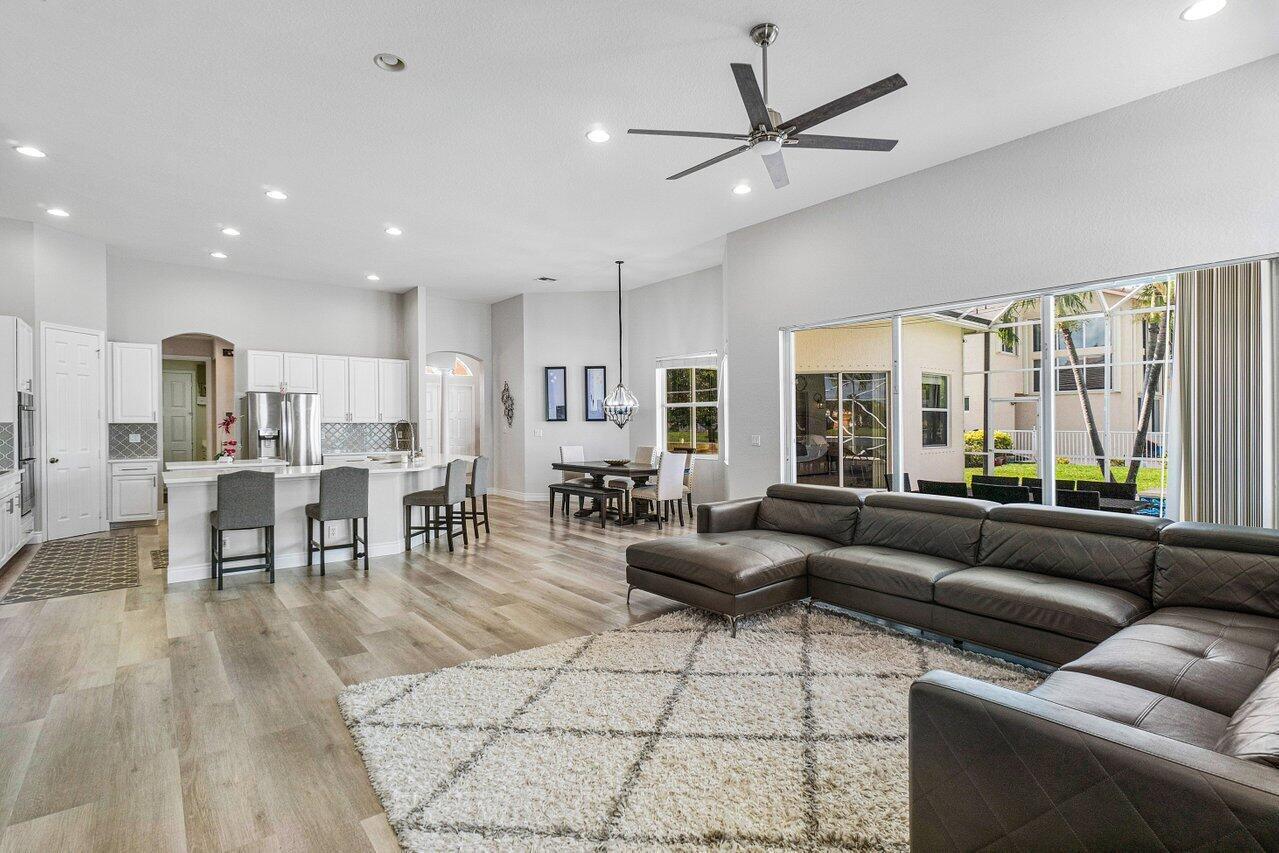 An open-concept living room and kitchen featuring light wood flooring and a large leather sectional — 11750 Osprey Pointe Circle, Wellington FL 33449, WELLINGTON, FL