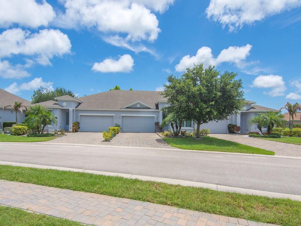 A street-level view of a light-colored duplex home with two garages and paved driveways — 6087 Scott Story Way, Vero Beach FL 32967, VERO BEACH, FL