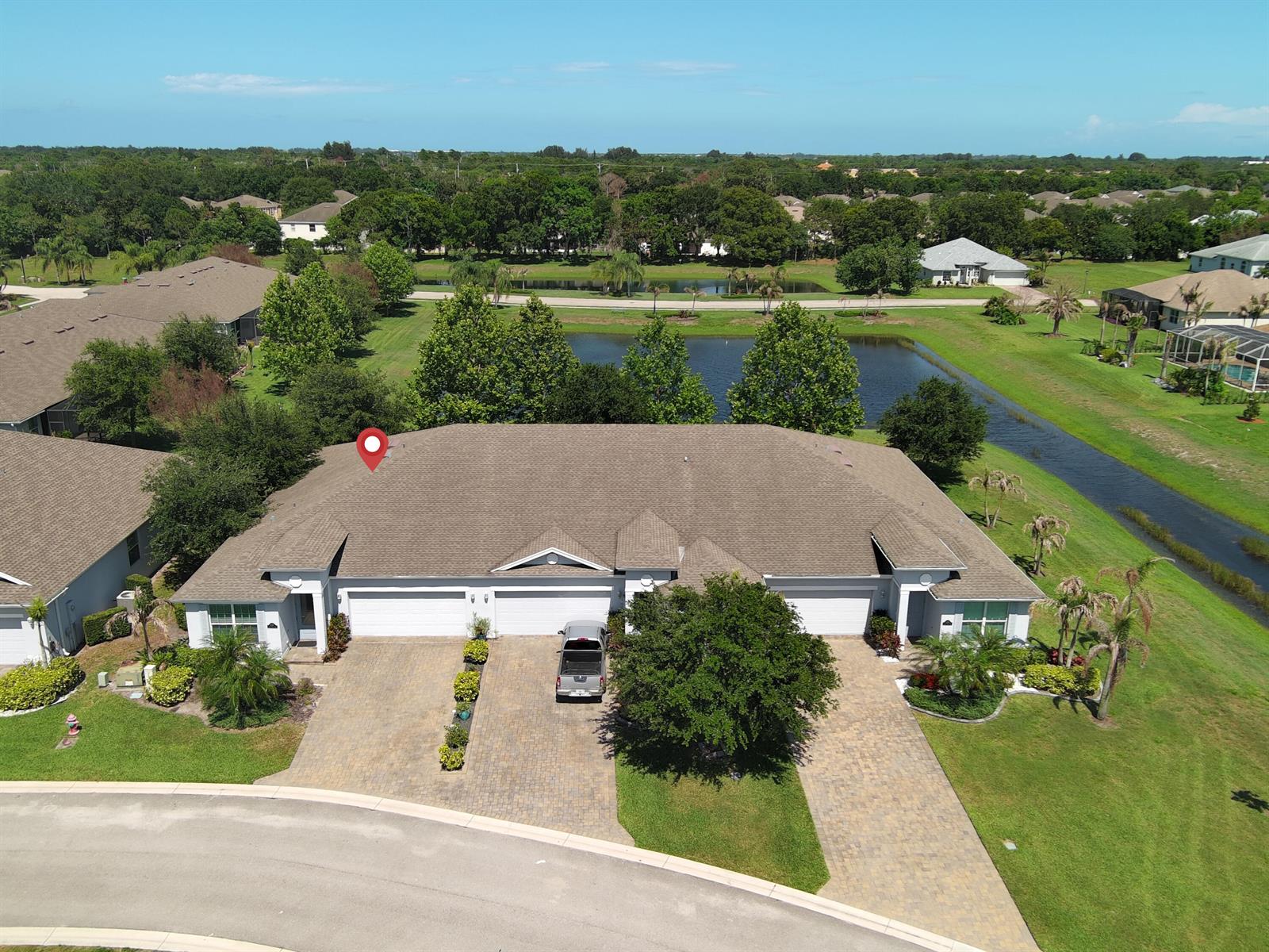An aerial view shows a duplex home with a paver driveway and a pond behind — 6087 Scott Story Way, Vero Beach FL 32967, VERO BEACH, FL