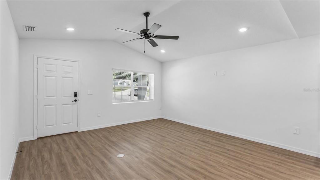 An empty room with wood-look flooring, a ceiling fan, and a white front door — 7540 WILLOW WISP DRIVE W, LAKELAND, FL