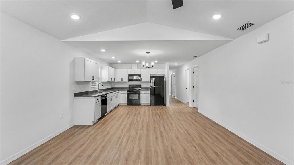 A kitchen with white cabinets, black appliances, and wood-look flooring in an open-concept space — 7540 WILLOW WISP DRIVE W, LAKELAND, FL