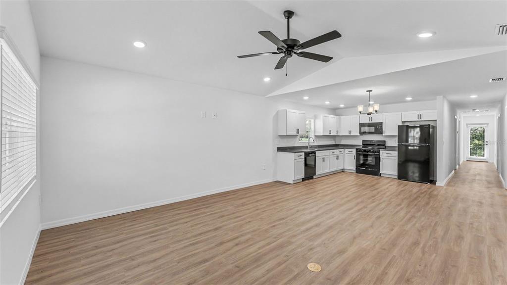 An open-concept kitchen and living area with white cabinets, black appliances, and wood-look flooring — 7540 WILLOW WISP DRIVE W, LAKELAND, FL