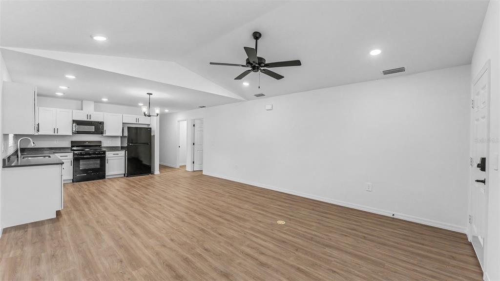 An open-concept kitchen and living area with white cabinets, black appliances, and wood-look flooring — 7540 WILLOW WISP DRIVE W, LAKELAND, FL