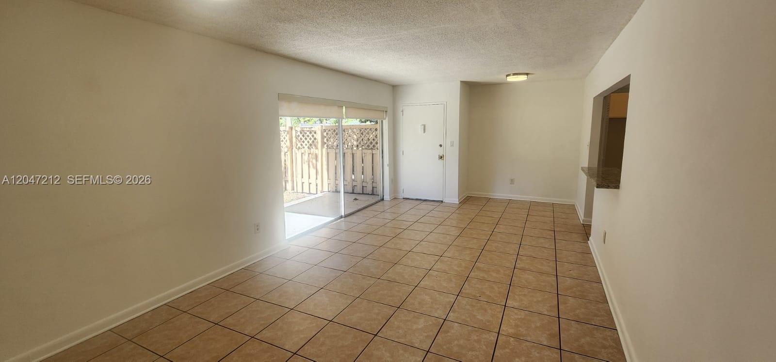An empty living room features beige tile flooring, white walls, and a sliding glass door — 4134 NW 79th Ave # 1C, Doral FL 33166, DORAL, FL