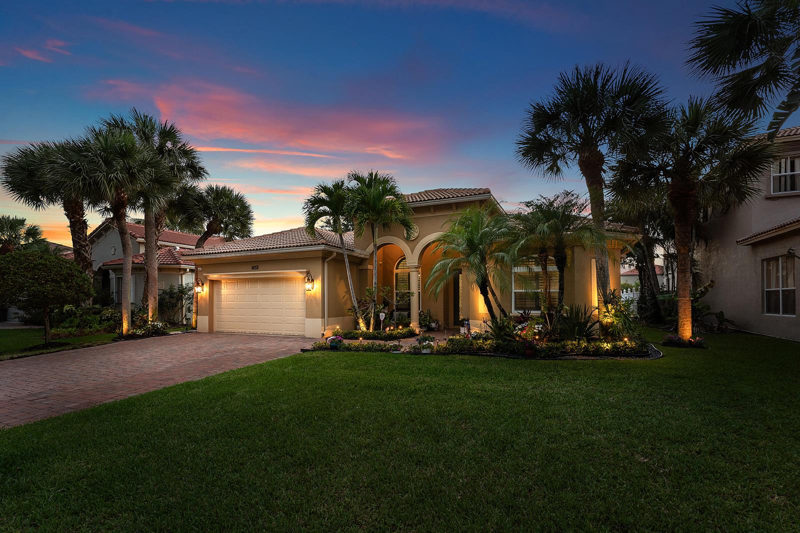 A single-story house with a two-car garage and palm trees at dusk — 1853 Palisades Drive, West Palm Beach FL 33411, WEST PALM BEACH, FL
