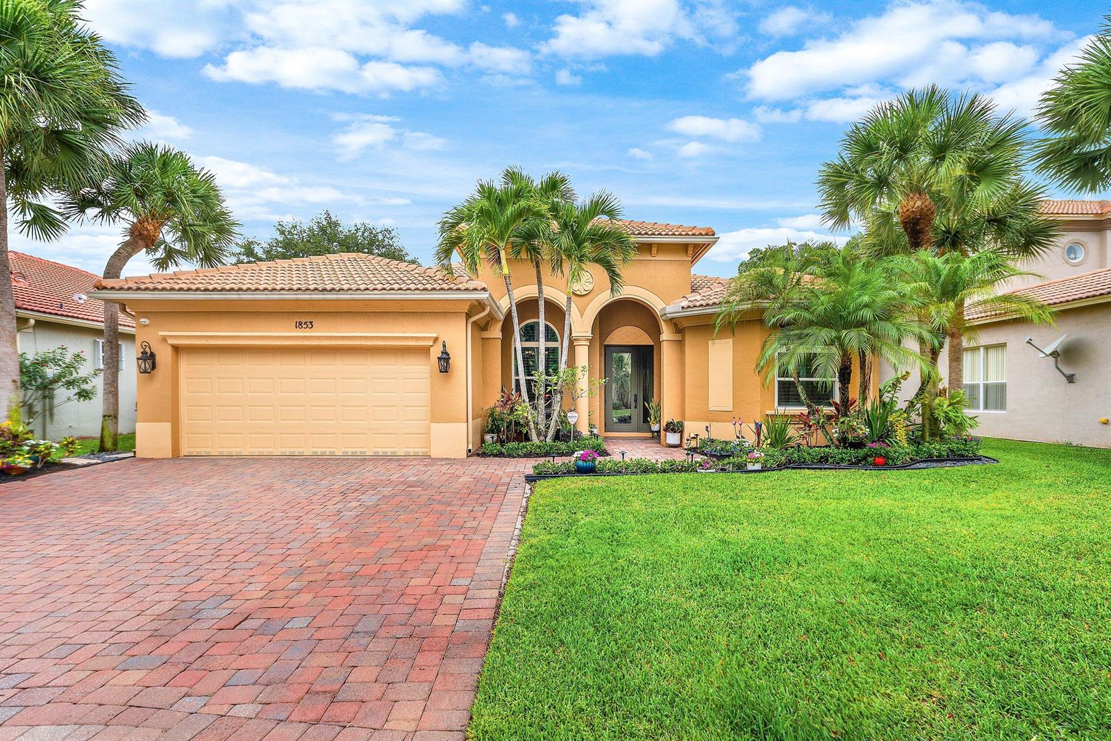 A single-story house with a tan stucco exterior, a brick driveway, and palm trees — 1853 Palisades Drive, West Palm Beach FL 33411, WEST PALM BEACH, FL
