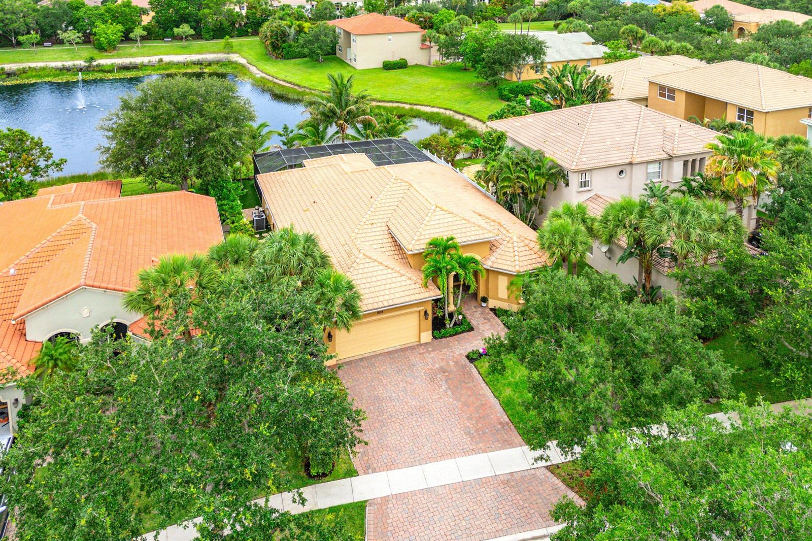 An aerial view shows a suburban house with a tiled roof, brick driveway, and pool cage — 1853 Palisades Drive, West Palm Beach FL 33411, WEST PALM BEACH, FL