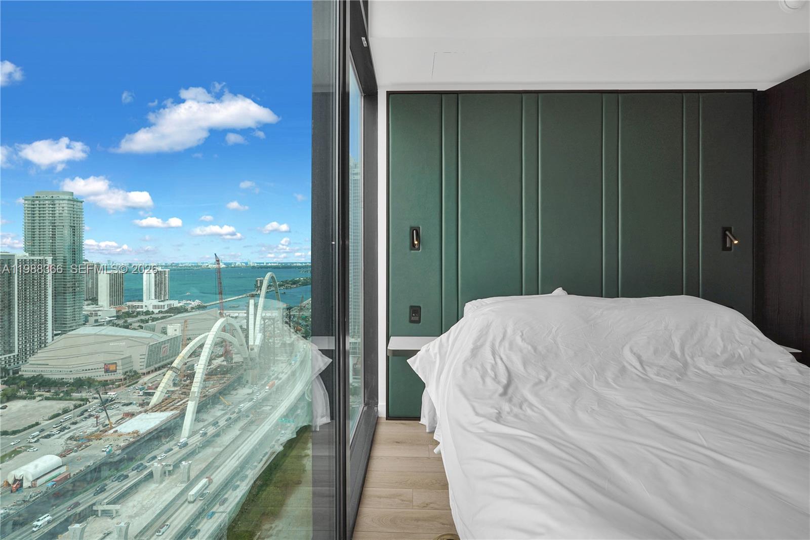 A bedroom features a green upholstered headboard wall and floor-to-ceiling windows overlooking a city skyline — 20 NE 11th St # 3603A, Miami FL 33132, MIAMI, FL