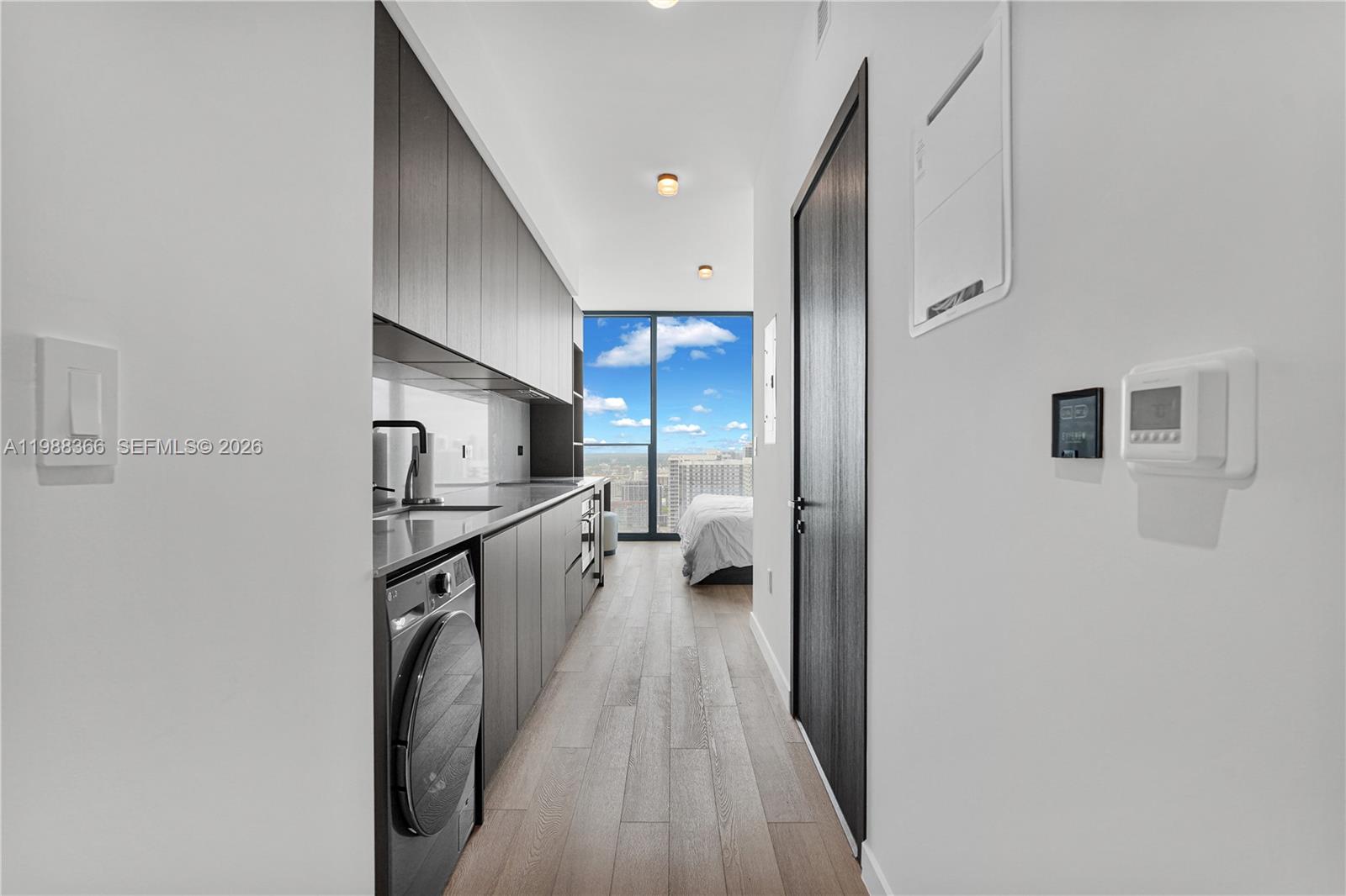 A narrow kitchen with dark cabinetry and a built-in washer leads to a bedroom area — 20 NE 11th St # 3603A, Miami FL 33132, MIAMI, FL