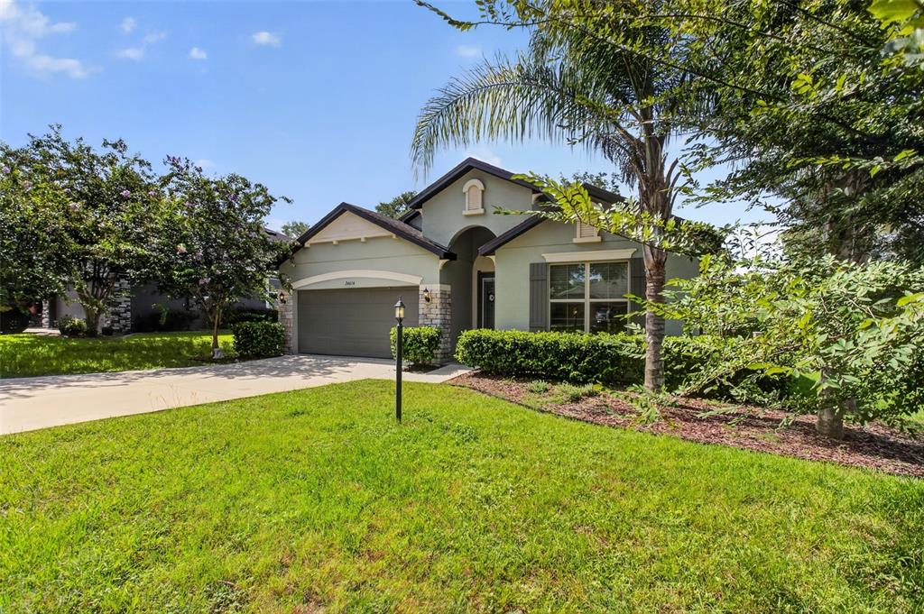 A single-story house with a two-car garage, light green siding, and a front lawn — 24414 WOODHILL COURT, SORRENTO, FL