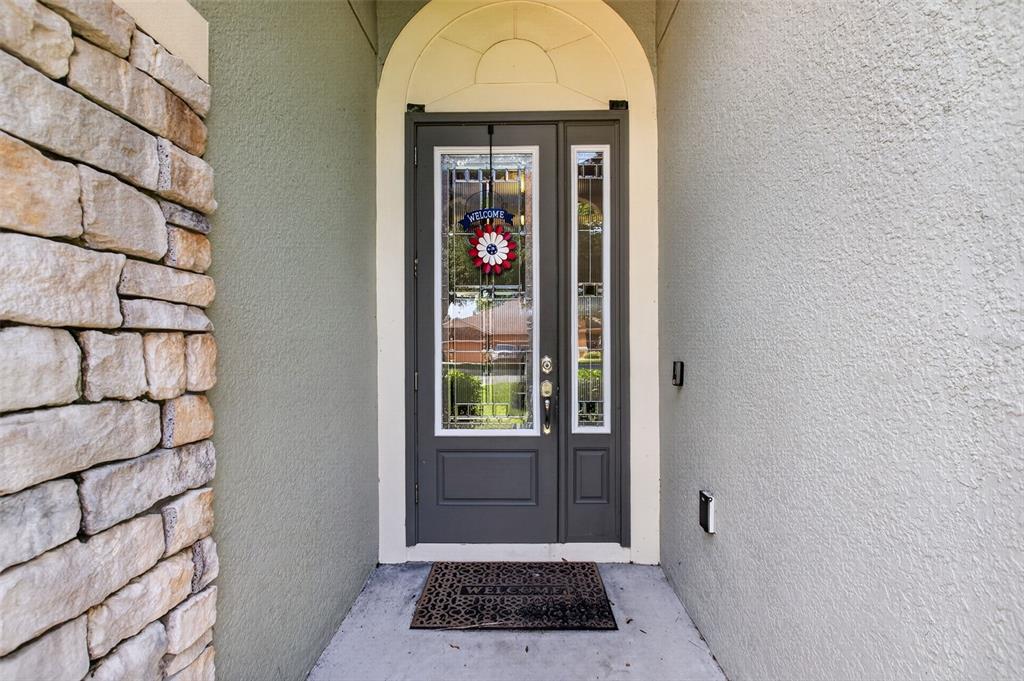 A dark gray front door with a glass insert and a stone-clad exterior wall — 24414 WOODHILL COURT, SORRENTO, FL