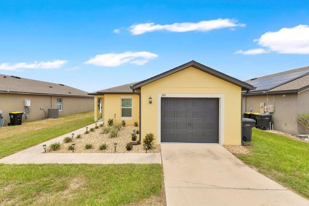 A single-story house with a yellow exterior, a gray garage door, and a concrete driveway — 392 KENSINGTON VIEW DRIVE, WINTER HAVEN, FL