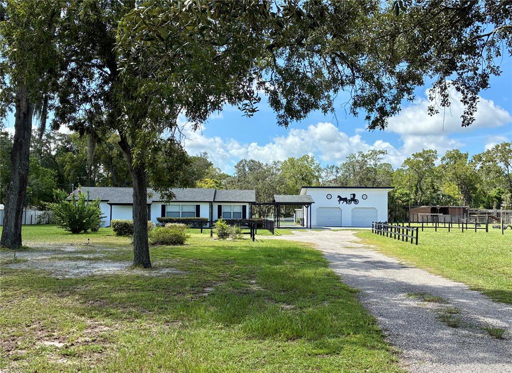 A white house and detached garage sit behind a black wooden fence on a grassy lot — 17620 CHORVAT AVENUE, SPRING HILL, FL