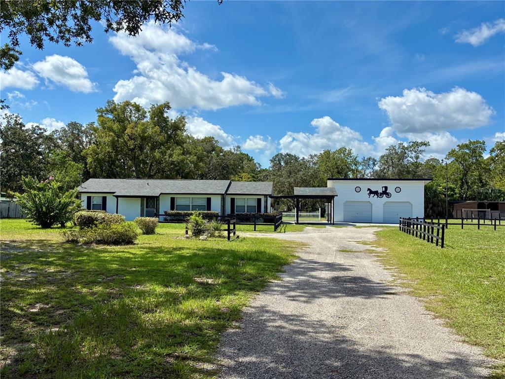 A single-story house with a gravel driveway, black fencing, and a detached two-car garage — 17620 CHORVAT AVENUE, SPRING HILL, FL