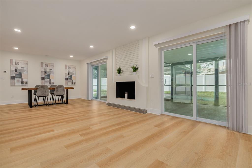 A bright living and dining area features light wood flooring, a fireplace, and sliding glass doors — 2065 ENVOY COURT, CLEARWATER, FL