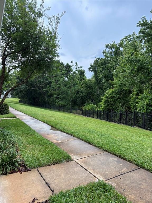 A concrete sidewalk runs alongside a grassy lawn bordered by a black metal fence — 304 SOUTHERN PECAN CIRCLE UNIT 208, WINTER GARDEN, FL