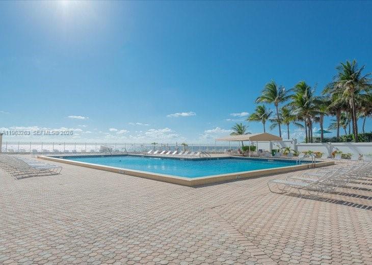 An outdoor swimming pool is surrounded by a paved deck and palm trees near the ocean — 3505 S Ocean Dr # 502, Hollywood FL 33019, HOLLYWOOD, FL