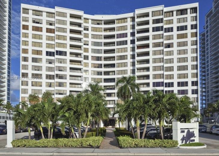 A multi-story white residential building with a curved facade stands behind palm trees and parking — 3505 S Ocean Dr # 502, Hollywood FL 33019, HOLLYWOOD, FL