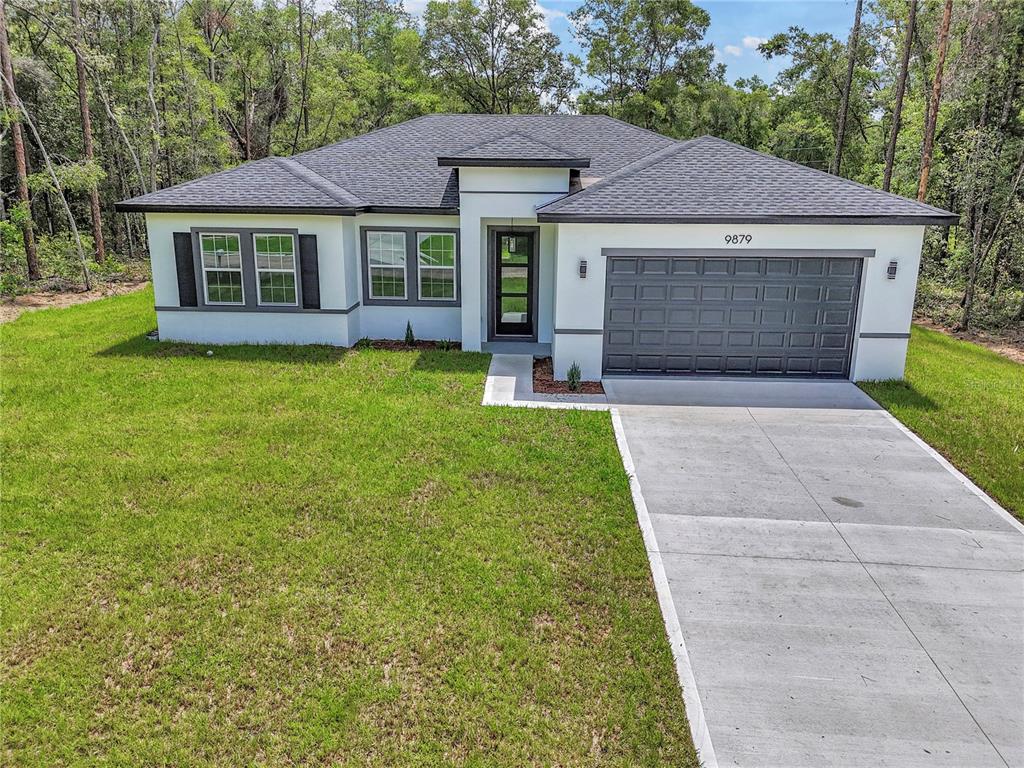 A single-story house with a gray roof, white stucco exterior, and a two-car garage — 9879 N CARAVEL TERRACE, DUNNELLON, FL