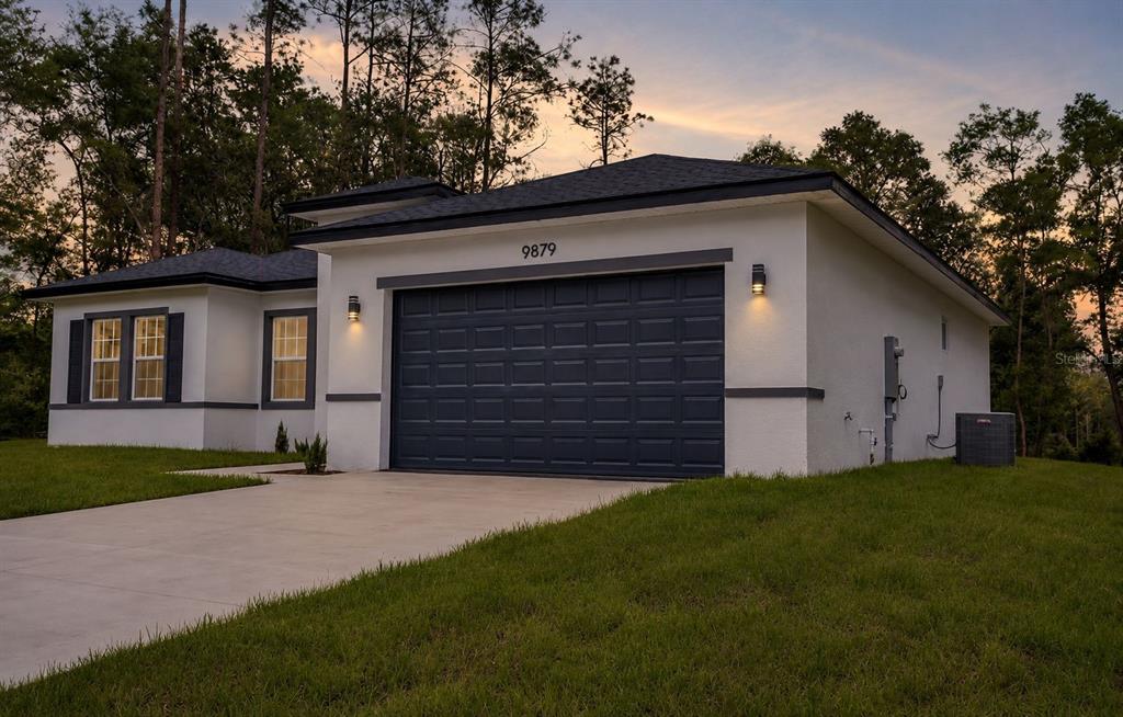 A single-story house with a white stucco exterior, dark trim, and a two-car garage — 9879 N CARAVEL TERRACE, DUNNELLON, FL