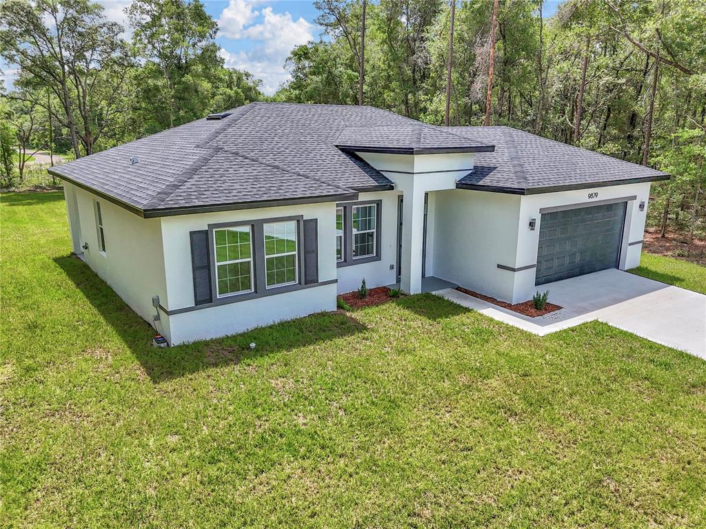 A single-story house with a white stucco exterior, dark roof, and attached two-car garage — 9879 N CARAVEL TERRACE, DUNNELLON, FL