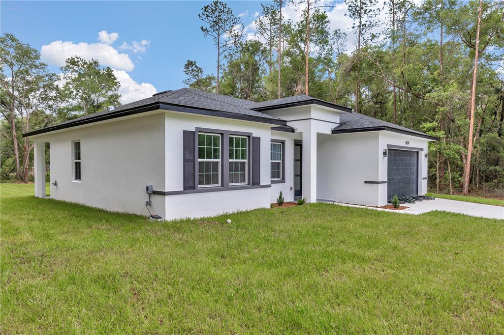 A modern, white single-story house with a dark roof, shutters, and an attached garage — 9879 N CARAVEL TERRACE, DUNNELLON, FL