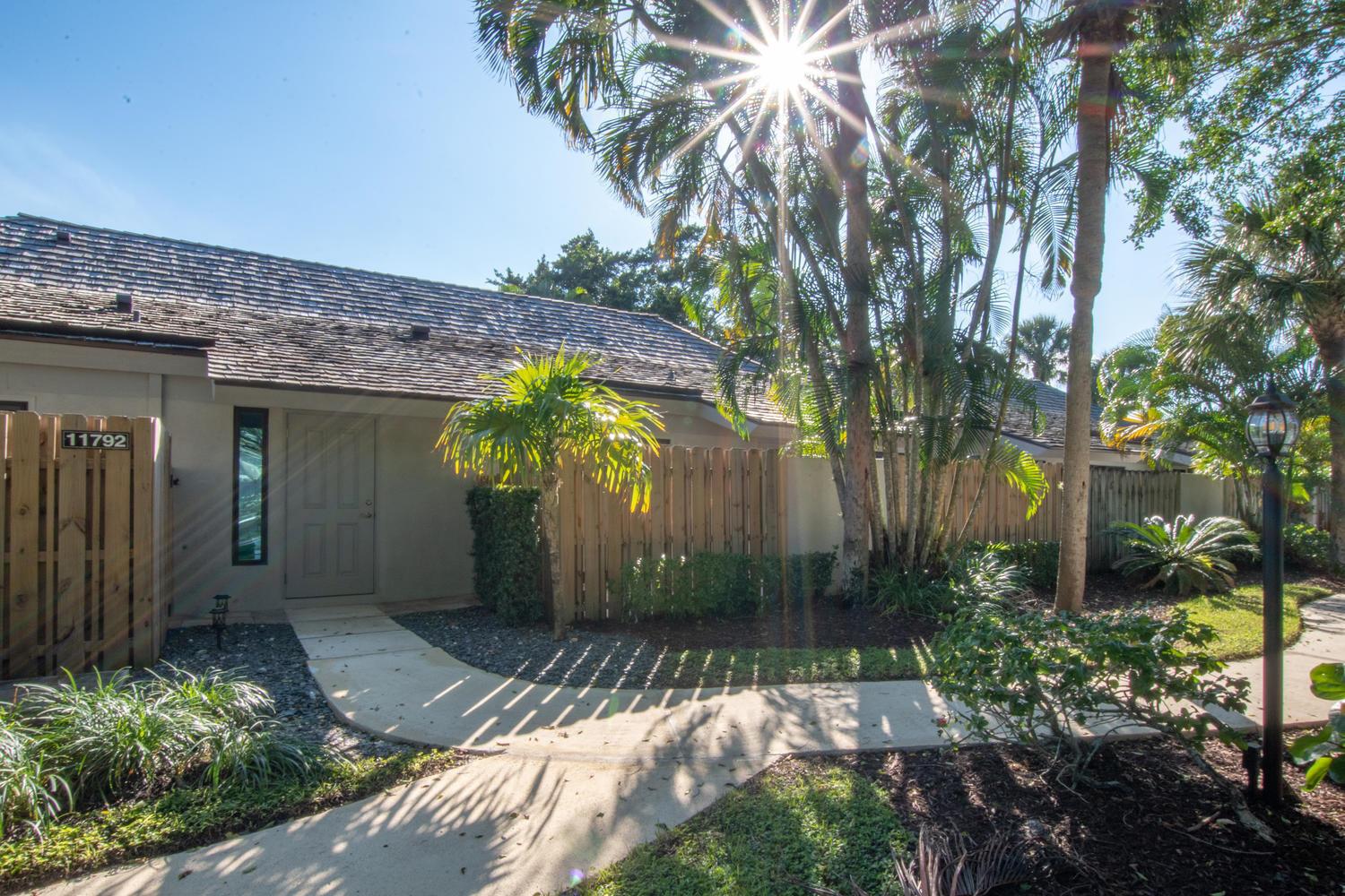 A concrete walkway leads to the front entrance of a house with a wooden fence — 11792 Wimbledon Circle, Wellington FL 33414, WELLINGTON, FL