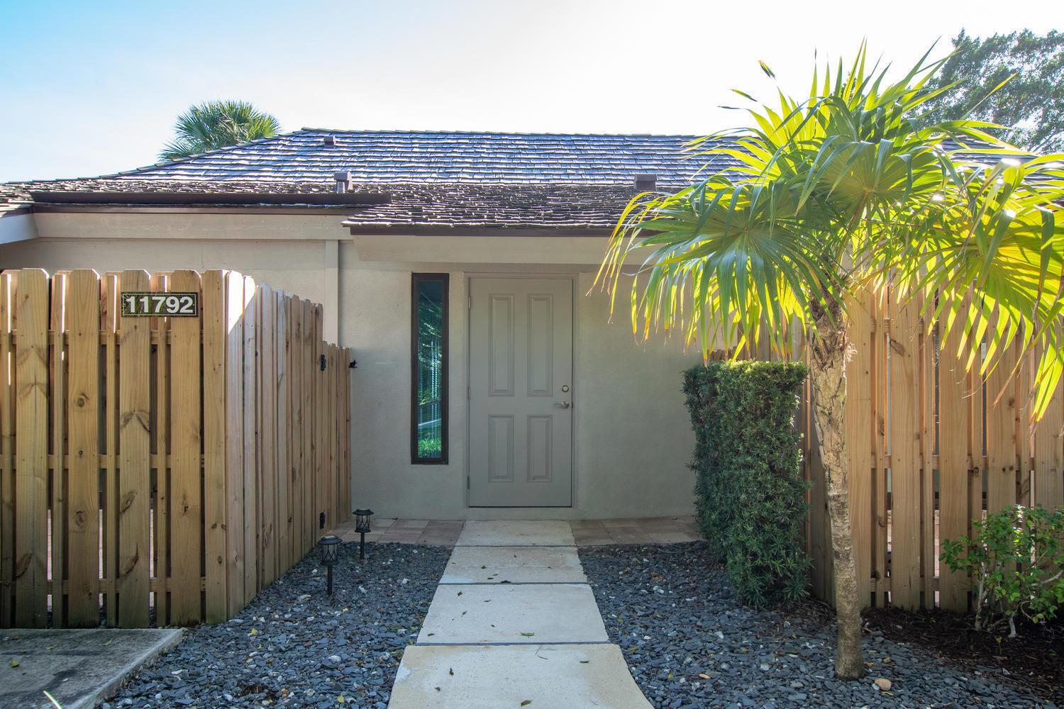 A beige front door with a side window is centered between two wooden privacy fences — 11792 Wimbledon Circle, Wellington FL 33414, WELLINGTON, FL