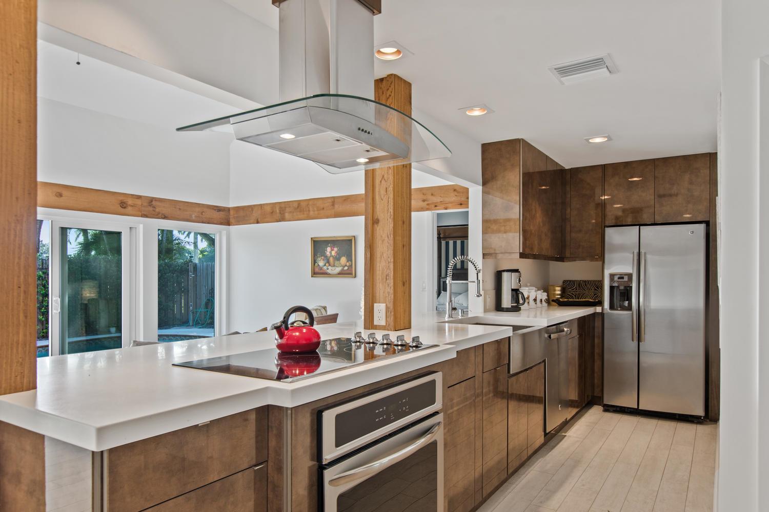 A modern kitchen features wood-toned cabinets, stainless steel appliances, a center island, and white countertops — 11792 Wimbledon Circle, Wellington FL 33414, WELLINGTON, FL