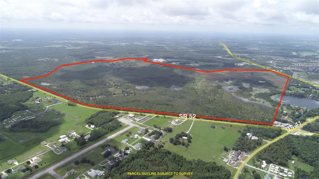 An aerial view shows a large, undeveloped parcel of land outlined in red near a highway — 19858 STATE ROAD 52, LAND O LAKES, FL