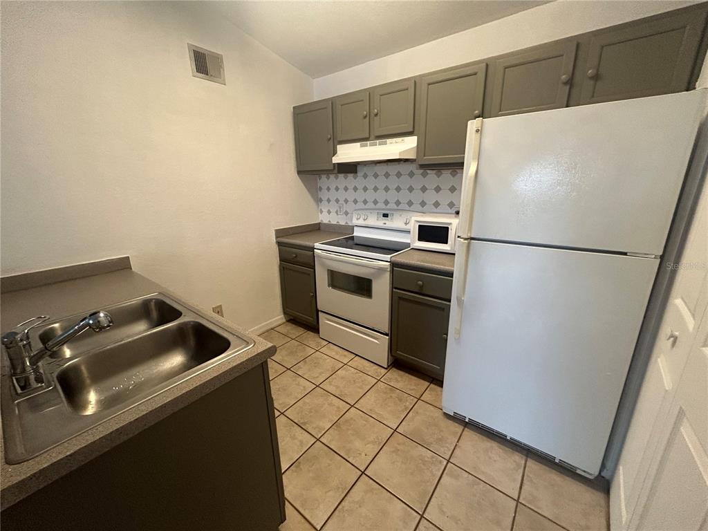 A kitchen features gray cabinets, white appliances, a double sink, and tiled flooring — 8939 LATREC AVENUE UNIT 1312, ORLANDO, FL