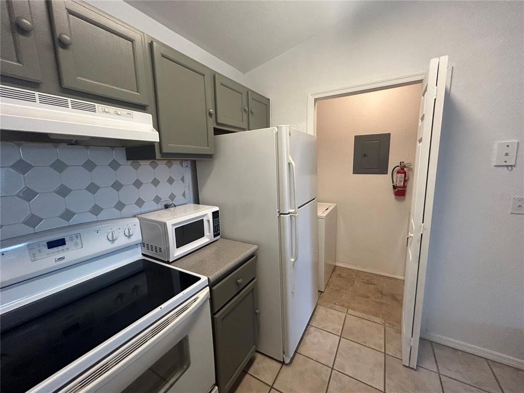 A kitchen features gray cabinets, a white stove, a microwave, and a doorway to a laundry area — 8939 LATREC AVENUE UNIT 1312, ORLANDO, FL