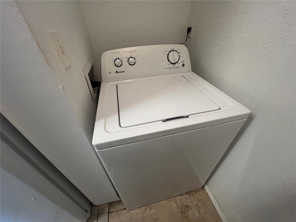 A white Amana top-loading washing machine sits in a small laundry closet — 8939 LATREC AVENUE UNIT 1312, ORLANDO, FL