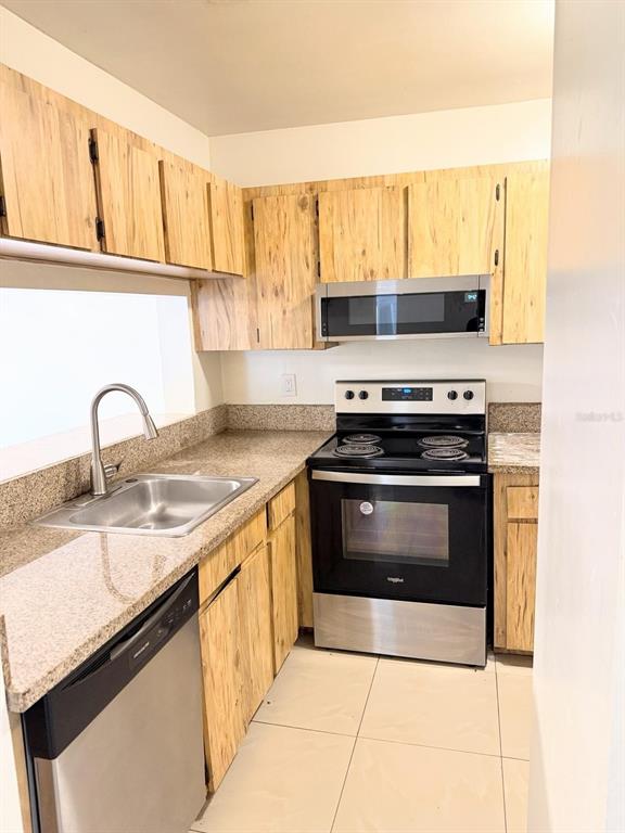 A kitchen features light wood cabinets, granite countertops, stainless steel appliances, and tile flooring — 5226 VIA HACIENDA CIRCLE UNIT A215, ORLANDO, FL
