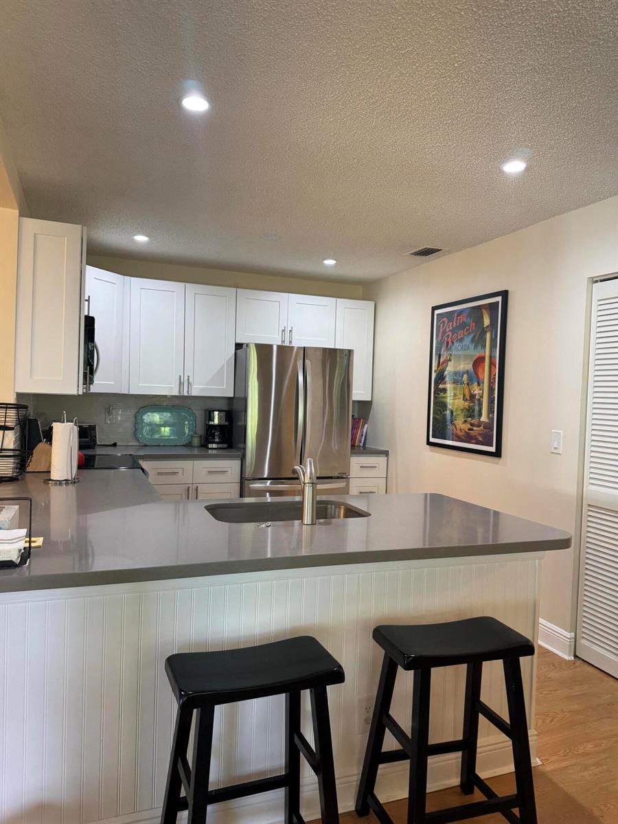 A kitchen features white cabinets, stainless steel appliances, a gray countertop, and two black stools — 108 Ocean Dunes Circle # 108, Jupiter FL 33477, JUPITER, FL