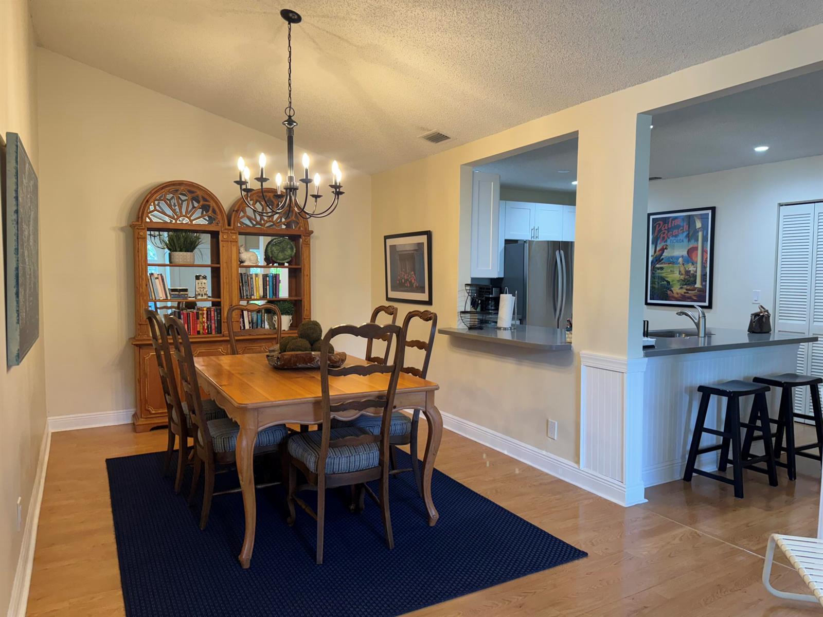 A dining room with a wooden table, hutch, and chandelier, adjacent to a kitchen pass-through — 108 Ocean Dunes Circle # 108, Jupiter FL 33477, JUPITER, FL