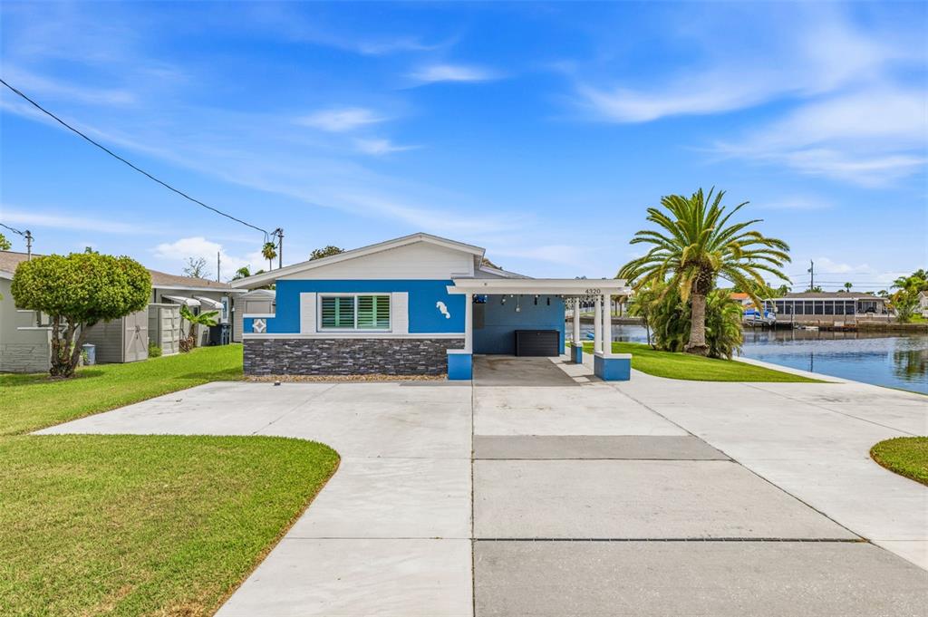 A blue house with a stone facade and a carport sits next to a canal — 4320 FLORAMAR TERRACE, NEW PORT RICHEY, FL